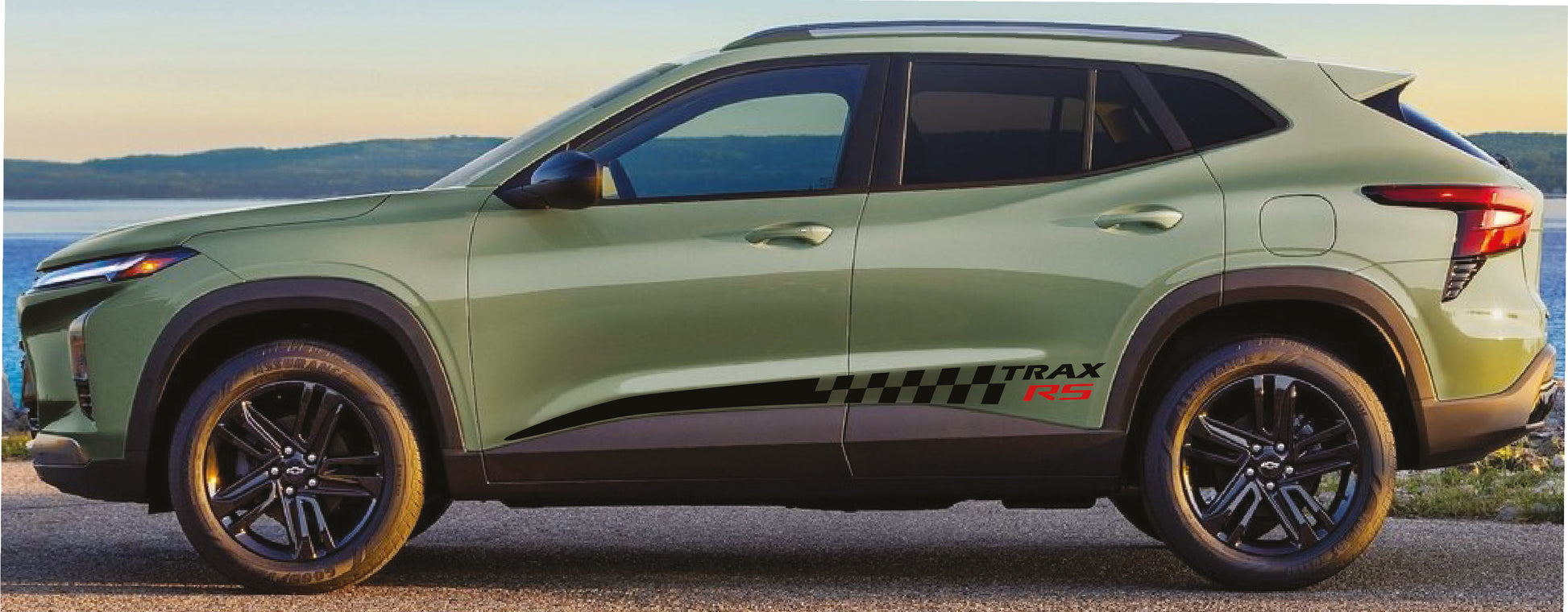 Green SUV parked by a body of water with mountains in the background
