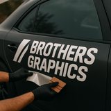 Person applying 'Brothers Graphics' vinyl decal to a car.