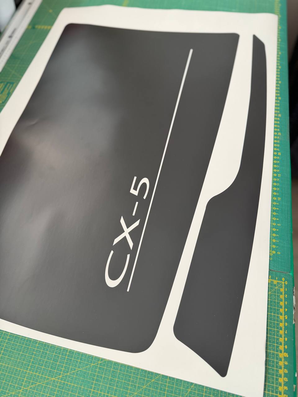 A black vinyl decal sheet with the text 'CX-5' and a white line, shown on a green cutting mat.
