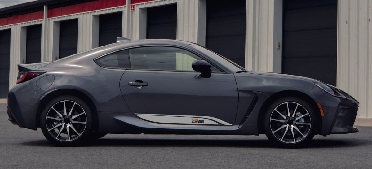 A dark gray Lexus RC F coupe with a white side stripe decal, parked in front of a garage building.