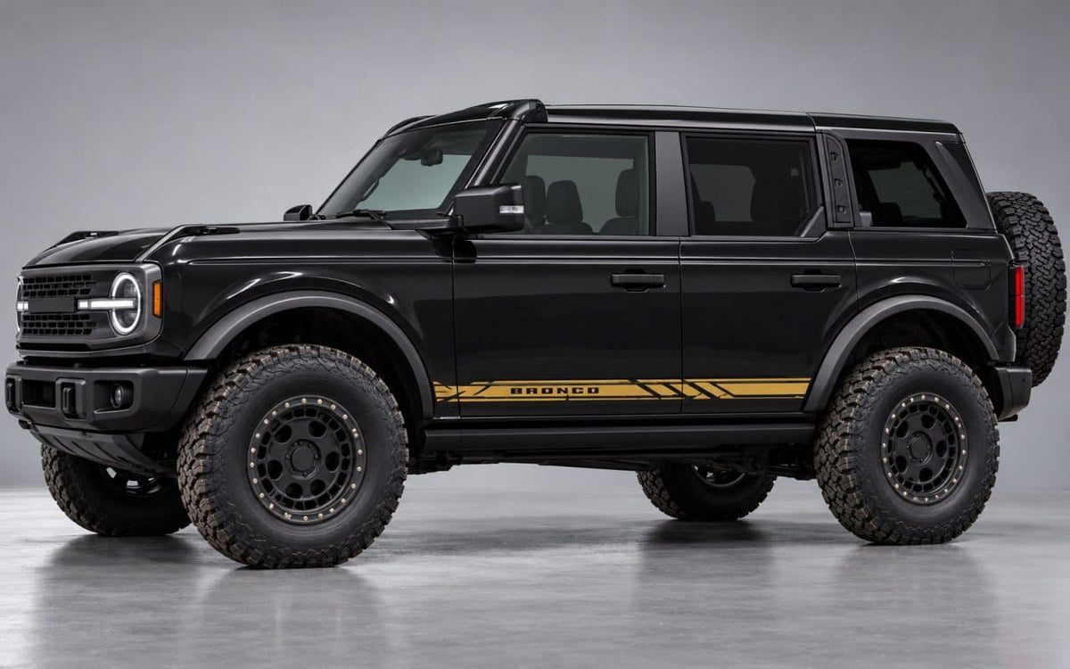 A black Ford Bronco SUV with gold side decals and black off-road tires, photographed in a studio setting against a gray background.