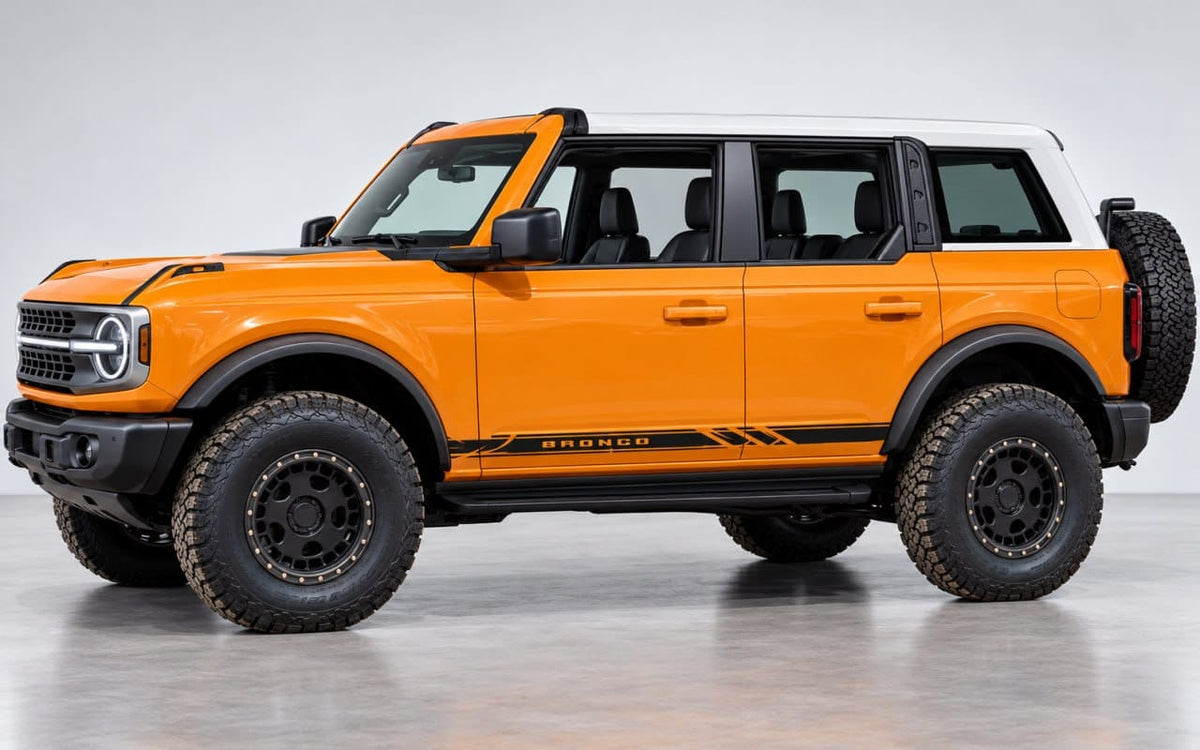 An orange Ford Bronco SUV with a white roof, black wheels, and off-road tires, photographed in a clean studio setting.