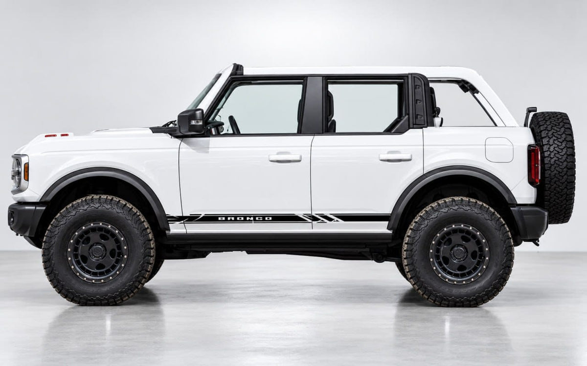 A white Ford Bronco with black off-road tires, black wheel rims, and a spare tire mounted on the rear door, shown in a side profile view on a light gray studio background.